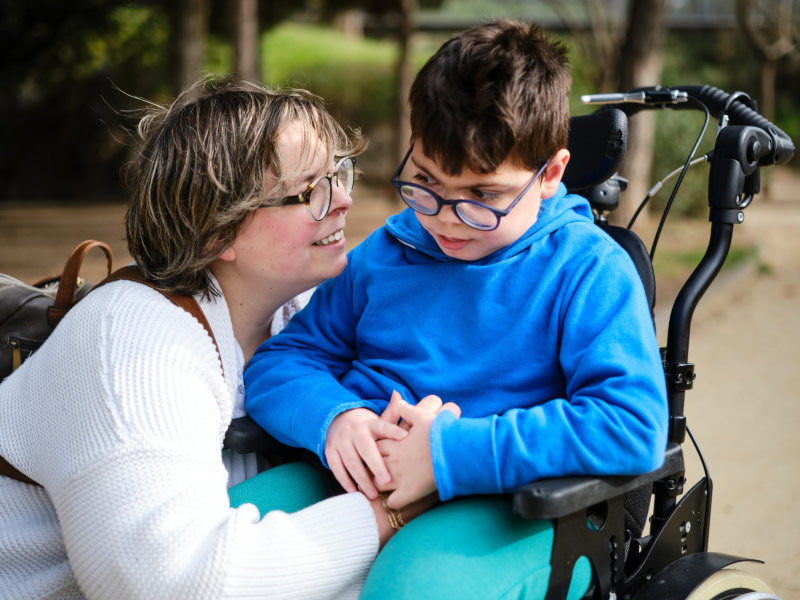 Disabled boy in a wheelchair enjoying a walk outdoors with his mother